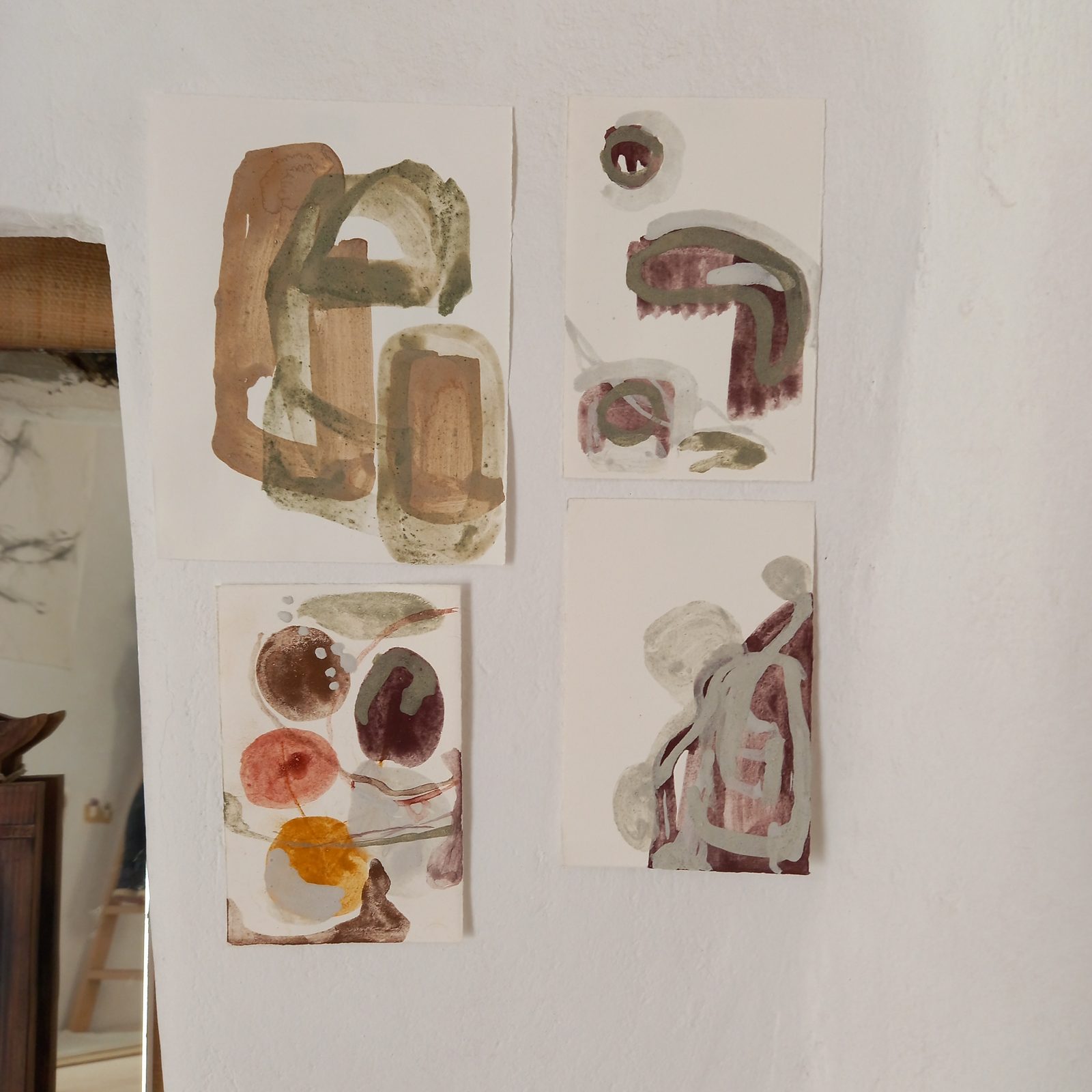 A cluster of earth-pigment drawings in ochre, red and purple pinned to the studio wall